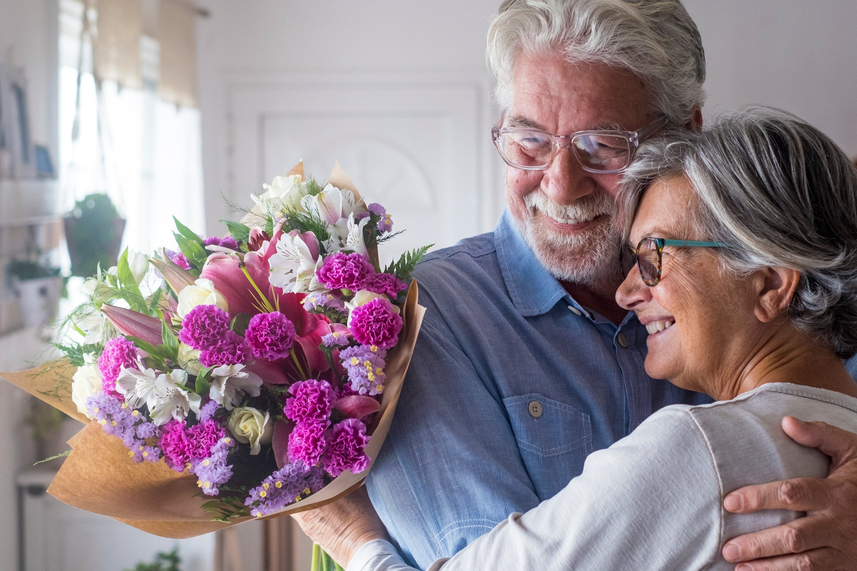 Old man giving flowers to his wife hugging him