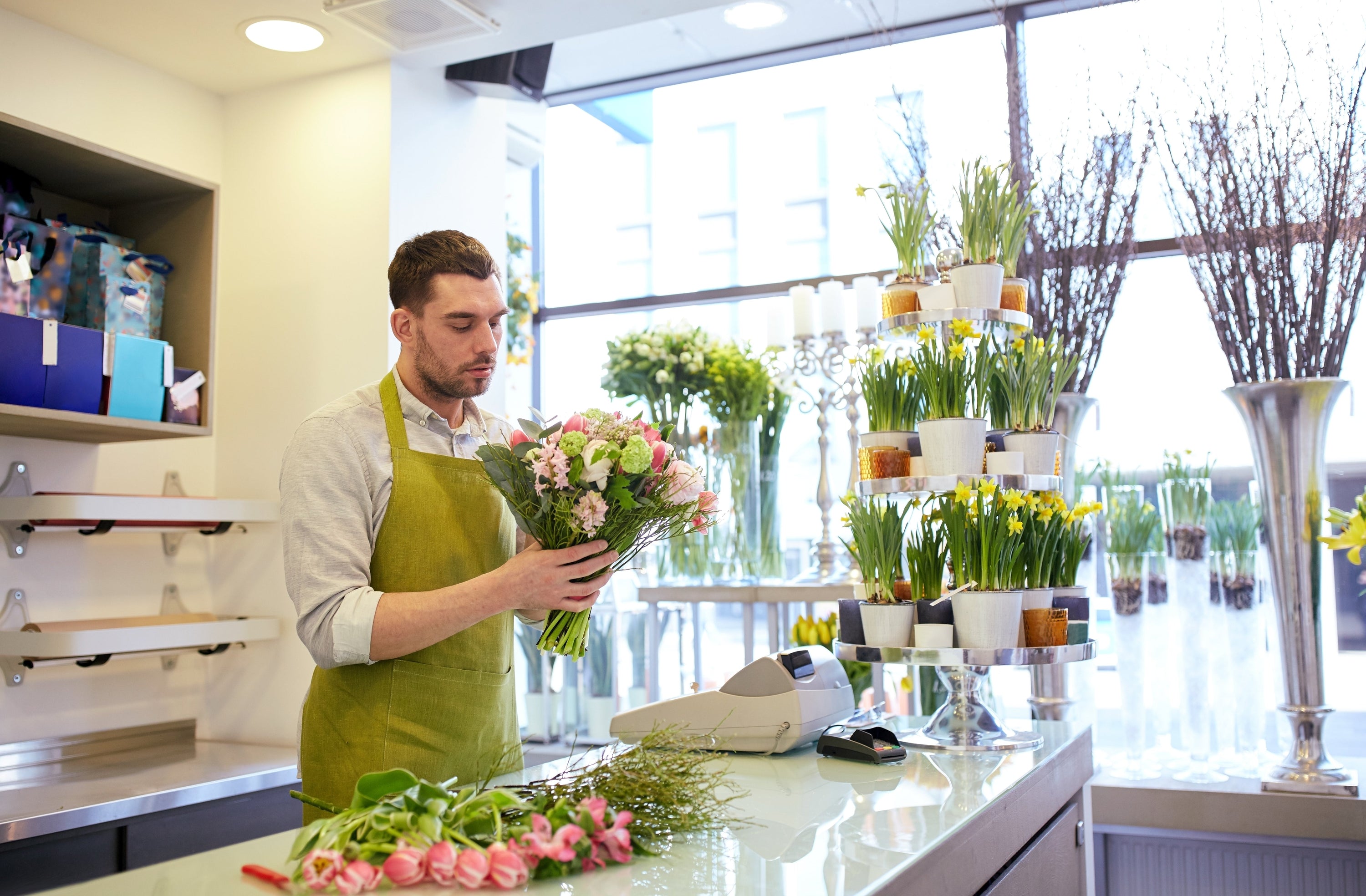 Male florist in his 30s putting together a bouquet of flowers in a well lit, clean shop.