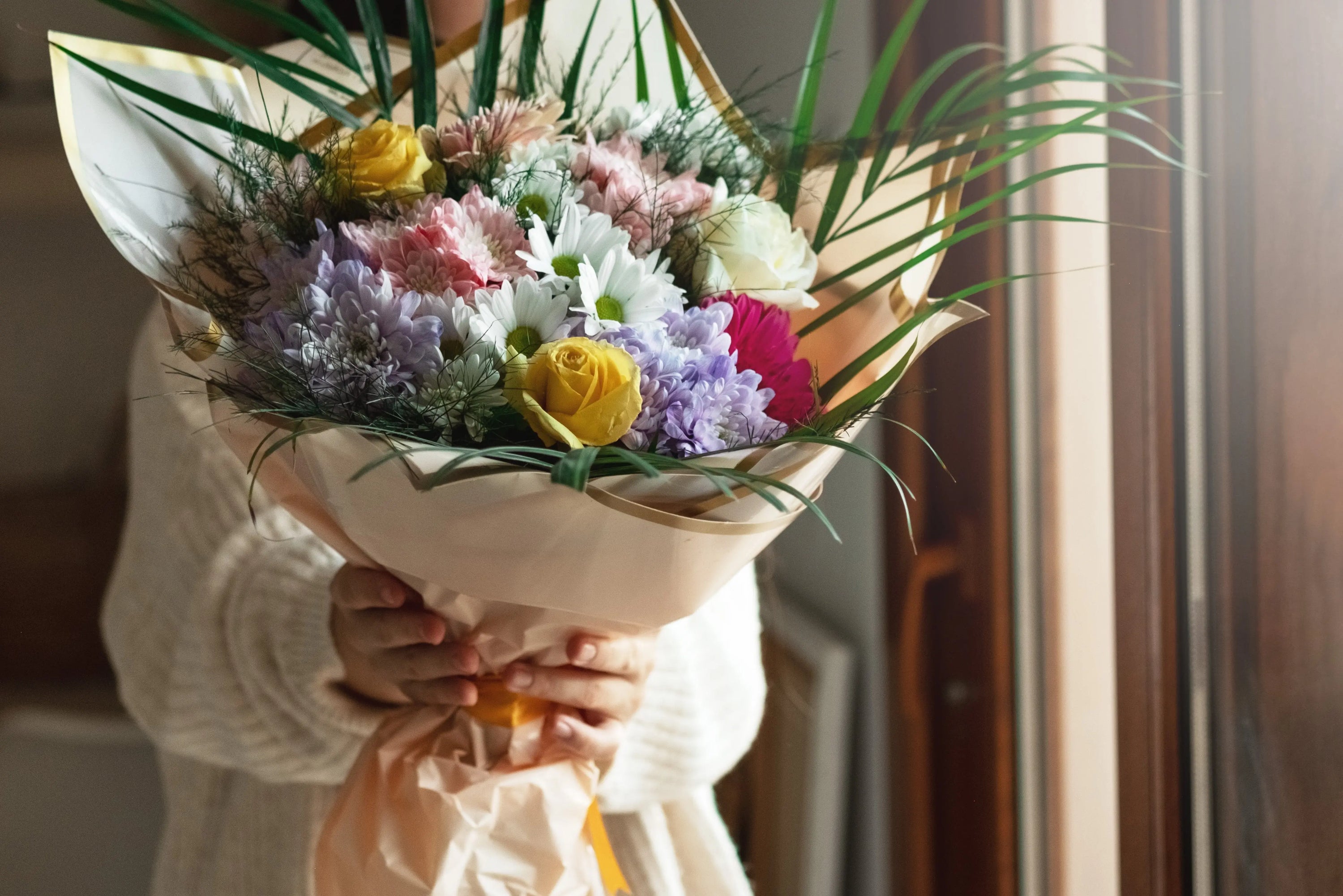 Woman is holding out a large wrapped bouquet consisting of an assortment of colorful flowers