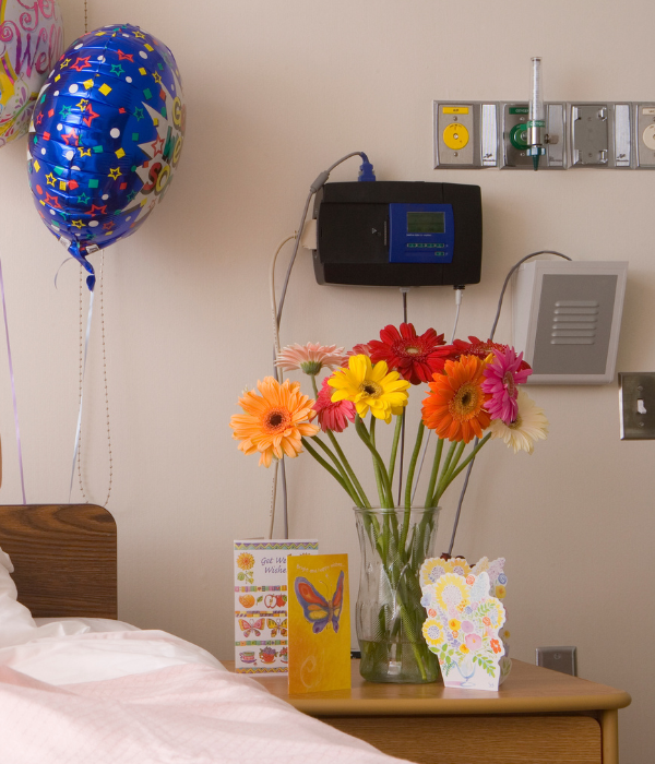Bright gerbera daisies and colourful cards on the side table of a hospital bed.