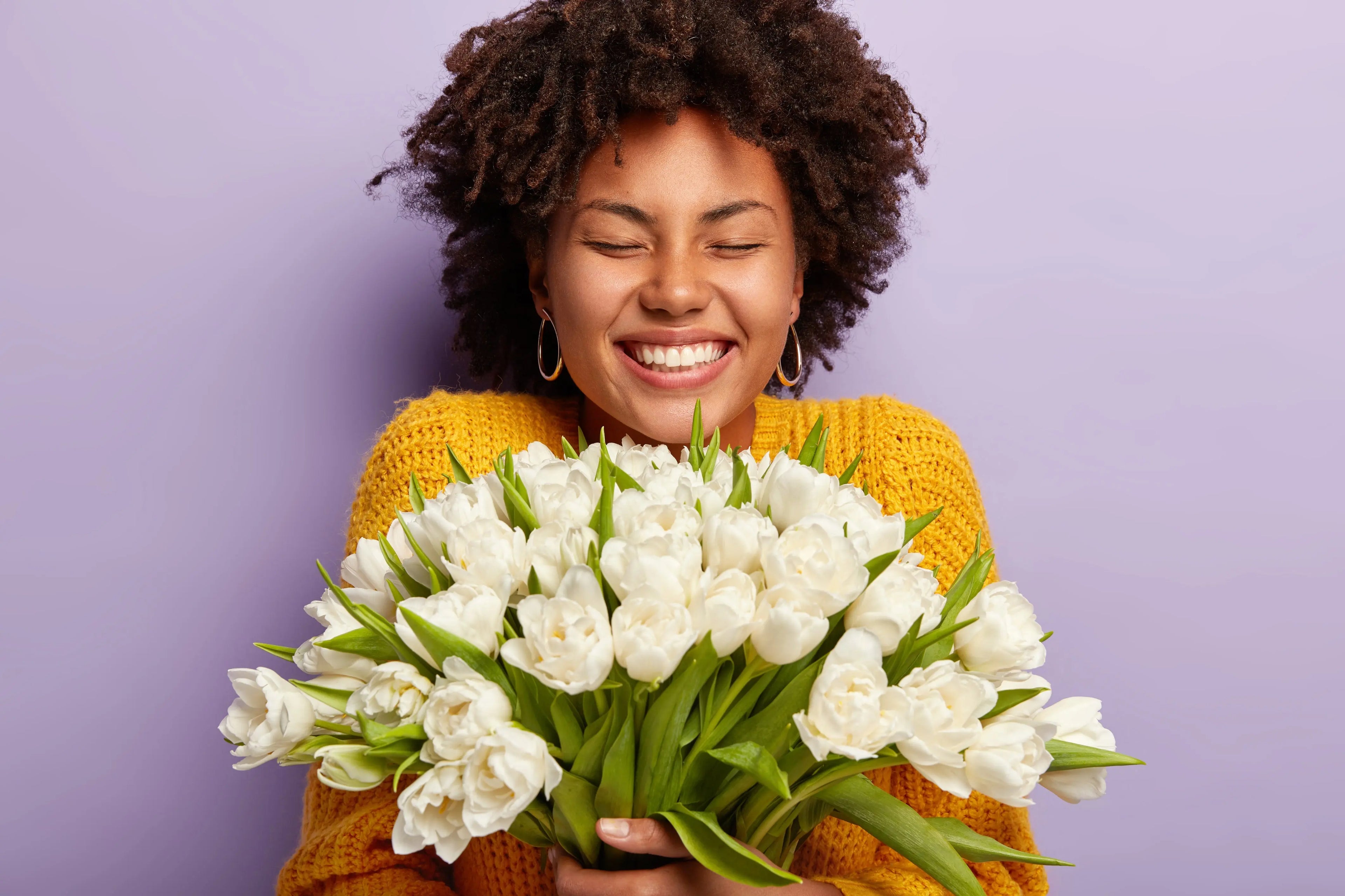 Woman with a wide smile holding tulips, against a purple background