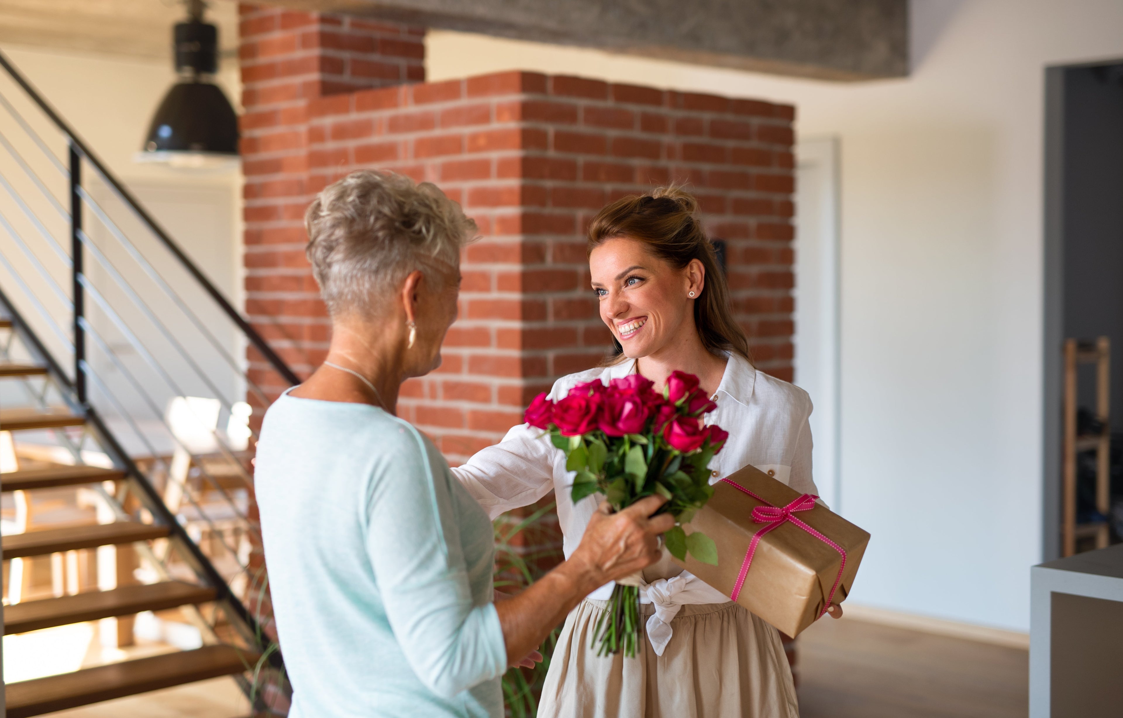 Adult woman receiving flowers and gift from her mom