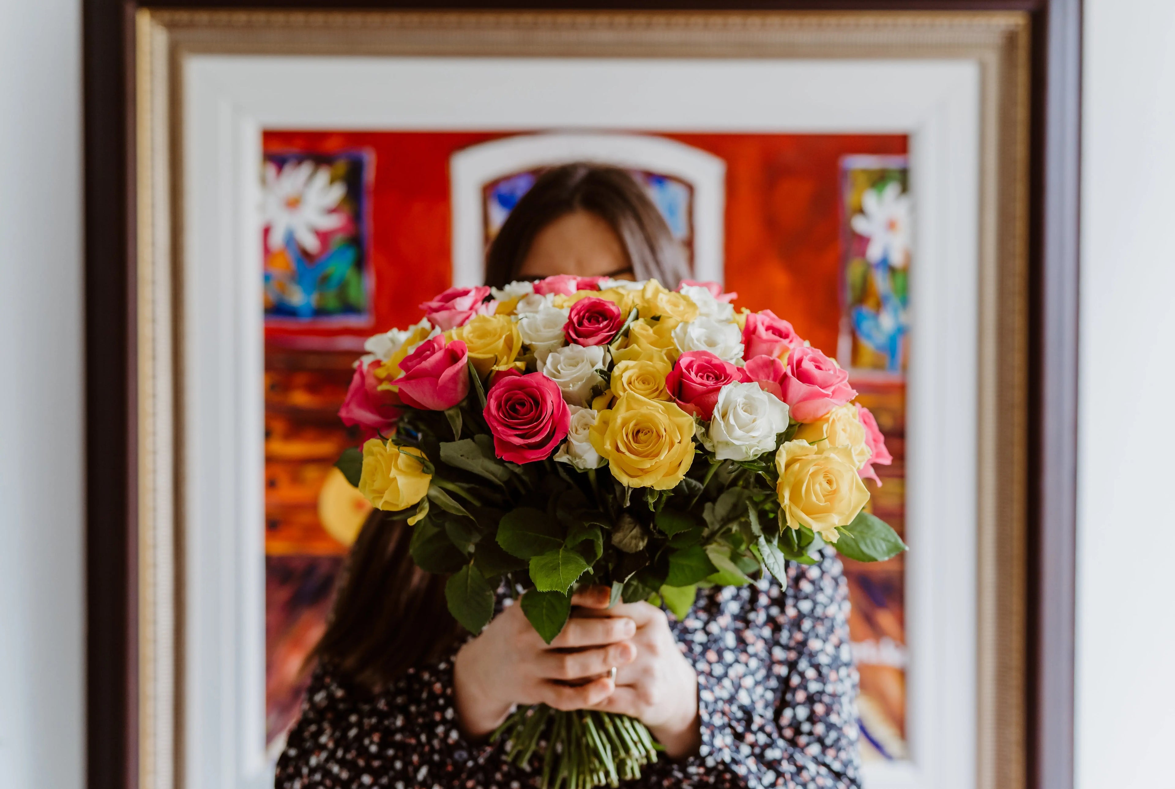 Woman holding up large bouquet of pink, yellow, and white roses. 